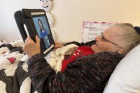 A photo of an elderly woman using a tablet to video call a mental health professional.