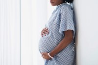 A photo of a pregnant Black woman holding her belly while wearing a hospital gown.